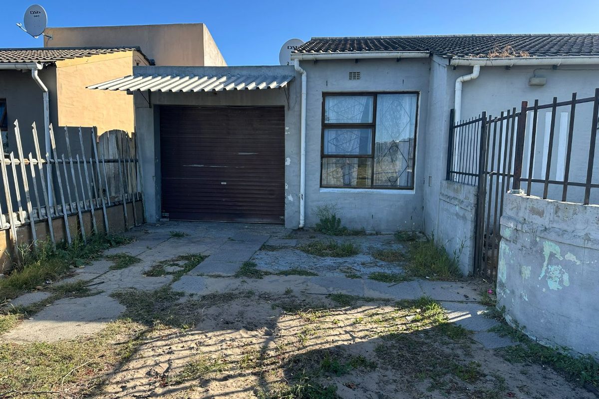 Front exterior view of a house featuring a single garage, metal security fencing, and a weathered concrete driveway requiring maintenance.