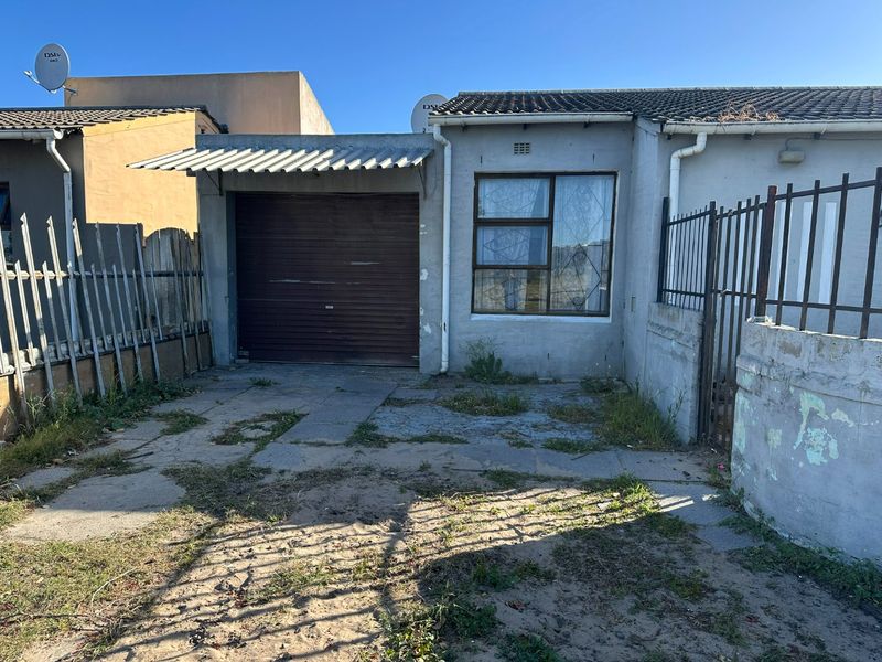 Front exterior view of a house featuring a single garage, metal security fencing, and a weathered concrete driveway requiring maintenance.