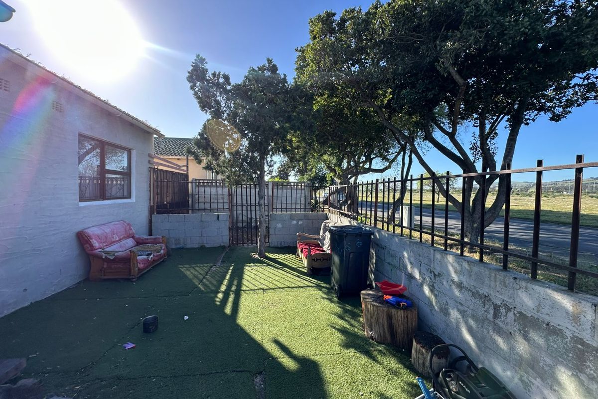 A rear outdoor area featuring a concrete boundary wall with metal fencing and artificial turf, offering potential for landscaping and improvement.