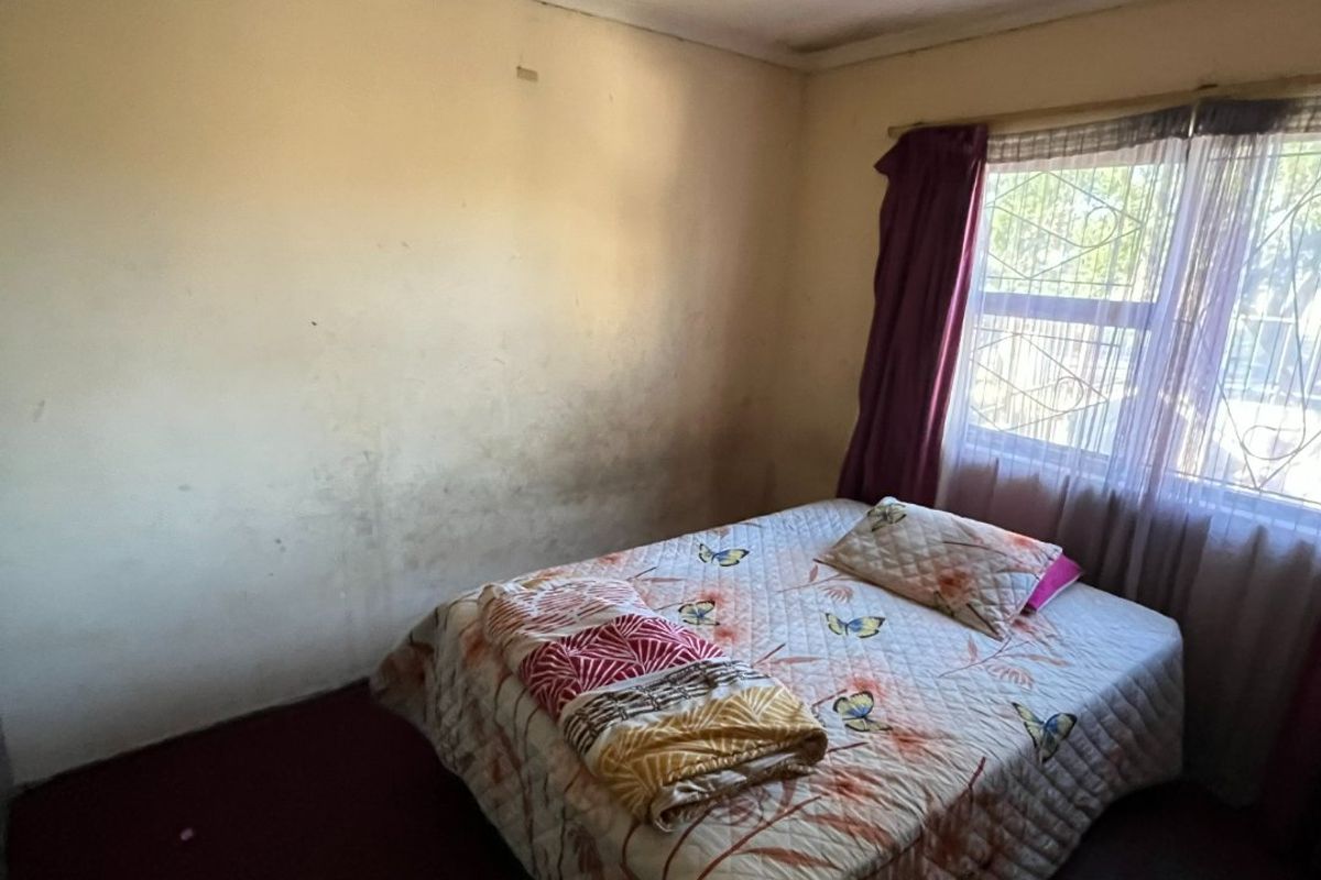 A bedroom featuring security burglar bars on the window, requiring cosmetic updates to the walls and flooring to improve its overall condition.