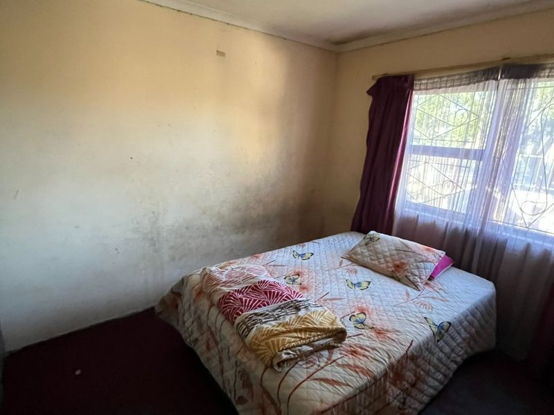 A bedroom featuring security burglar bars on the window, requiring cosmetic updates to the walls and flooring to improve its overall condition.