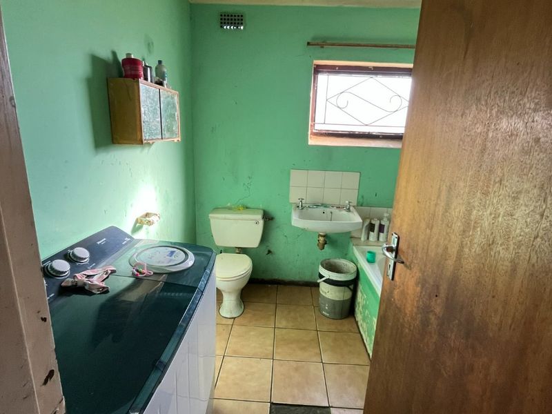 A laundry room featuring a toilet and wall-mounted basin, requiring significant renovation and repair to the flooring, walls, and ceiling finishes.