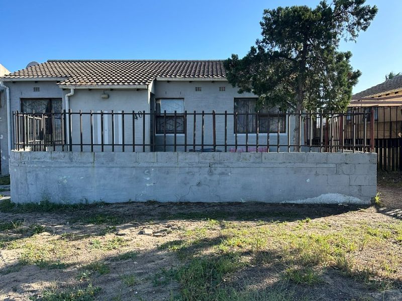 Front elevation of a single-story house featuring a concrete boundary wall, metal security fencing, and tiled roof, set on an unlandscaped plot.