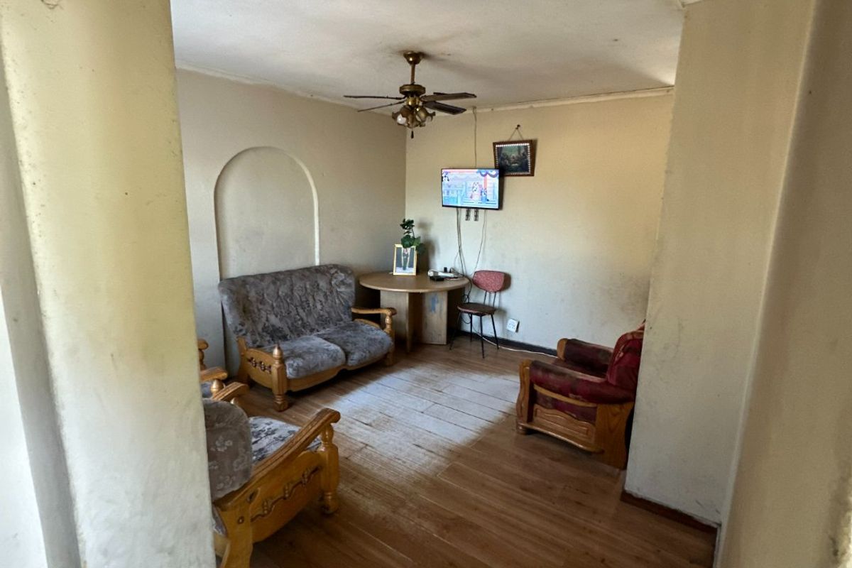 A living room featuring laminate flooring, a ceiling fan, and a decorative wall niche, currently showing signs of wear and requiring cosmetic updates.