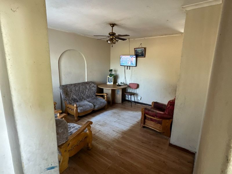 A living room featuring laminate flooring, a ceiling fan, and a decorative wall niche, currently showing signs of wear and requiring cosmetic updates.