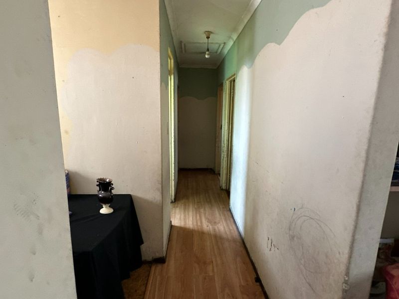 A narrow hallway featuring laminate flooring and coving, currently requiring cosmetic updates including wall repairs and repainting to improve the overall aesthetic.