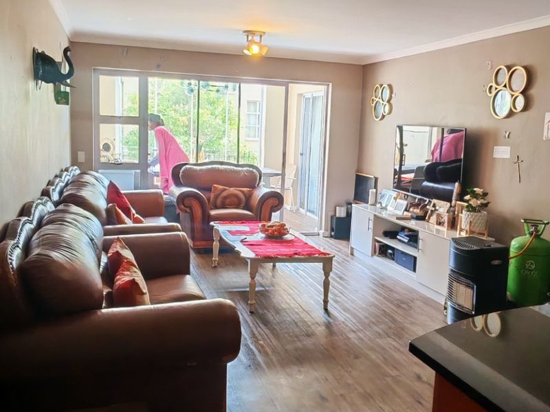 A spacious living room featuring laminate flooring, neutral wall tones, and a large sliding glass door providing access to the outdoor area.