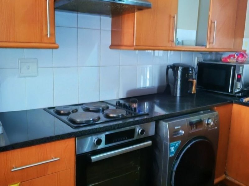 A functional kitchen featuring warm-toned laminate cabinetry, black granite countertops, a built-in oven with electric hob, and a tiled splashback.