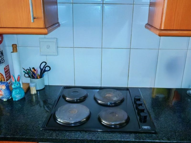 A functional kitchen area featuring wooden cabinetry, a granite countertop, a built-in oven, and an electric hob with an overhead extractor fan.