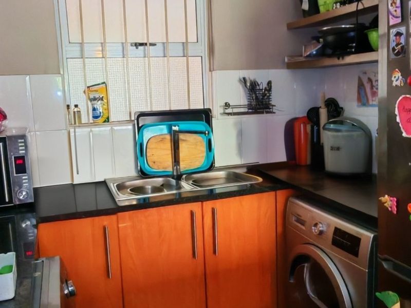 A compact kitchen featuring laminate cabinetry, double bowl sink, tiled backsplash, and security bars on the window.