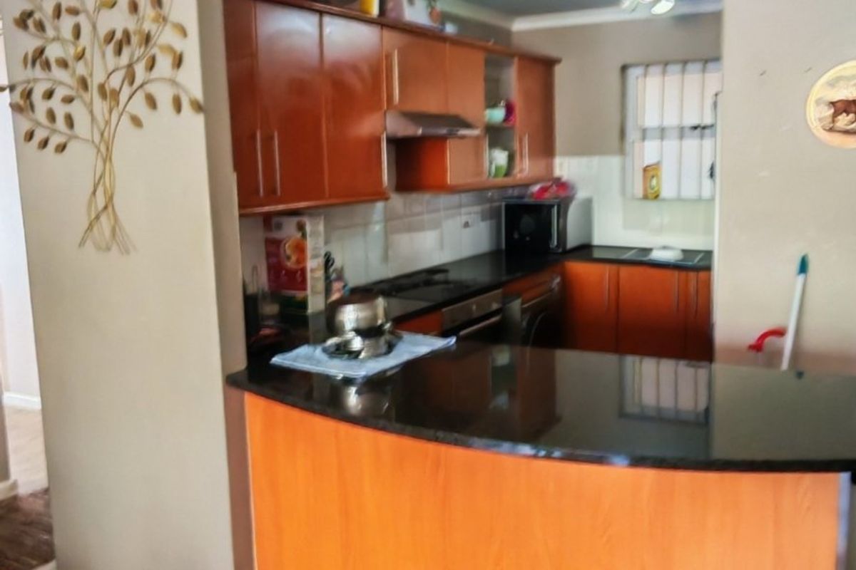 A functional kitchen featuring warm-toned laminate cabinetry, dark granite countertops, a breakfast bar, and integrated appliances, set against a wood-look laminate floor.