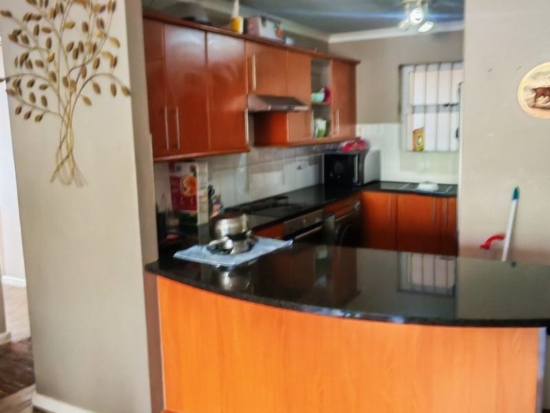 A functional kitchen featuring warm-toned laminate cabinetry, dark granite countertops, a breakfast bar, and integrated appliances, set against a wood-look laminate floor.