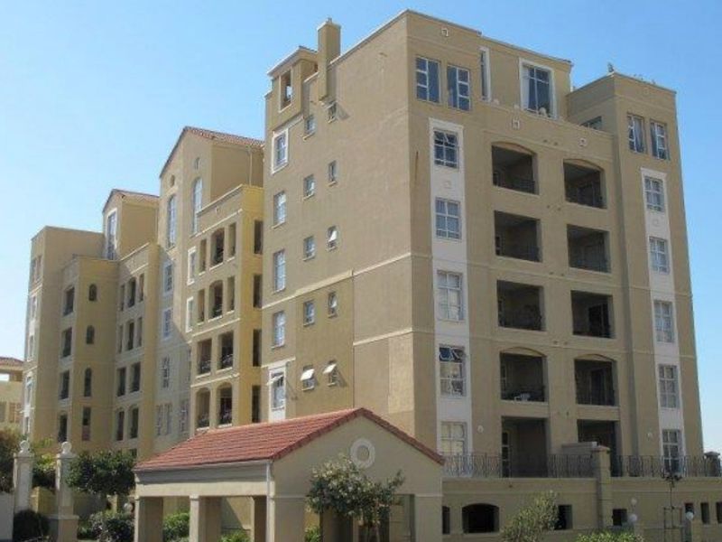 A multi-story apartment building featuring a beige facade, multiple balconies, and a covered entrance portico with a tiled roof.