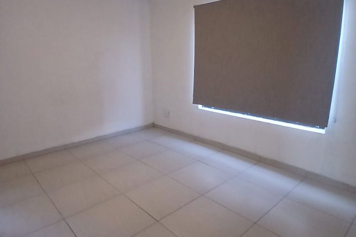 A clean, empty bedroom featuring neutral tiled flooring, a ceiling fan, and a fitted roller blind.
