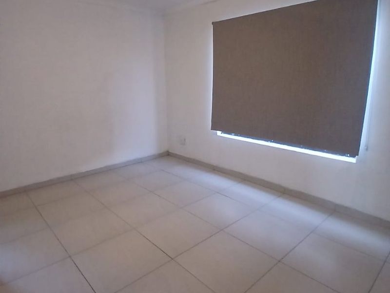 A clean, empty bedroom featuring neutral tiled flooring, a ceiling fan, and a fitted roller blind.