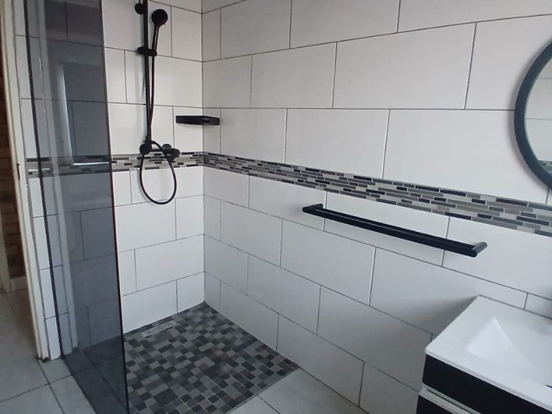 Modern bathroom featuring a walk-in shower with black fixtures, subway wall tiling, mosaic floor accents, and a sleek vanity cabinet.