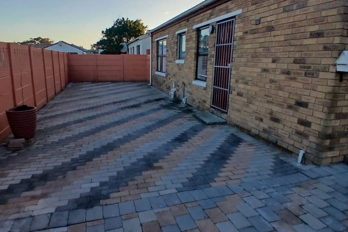 A rear exterior view featuring a brick facade, paved patio area, and secure boundary walling.