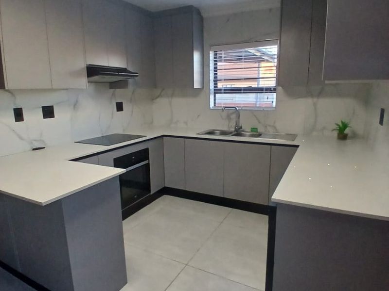 Modern U-shaped kitchen featuring grey cabinetry, white quartz countertops, marble-look splashbacks, integrated appliances, and large format floor tiles.