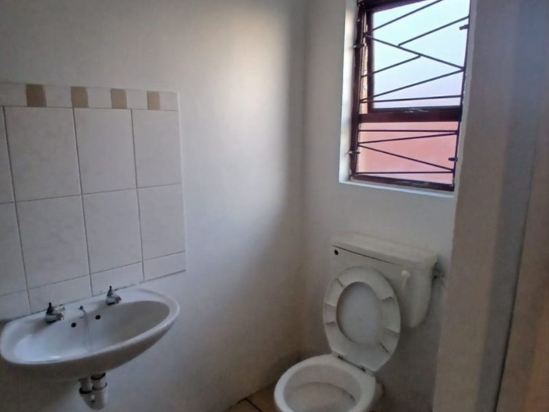 A compact bathroom featuring a wall-mounted basin, tiled splashback, and a standard toilet, with security bars installed on the window.