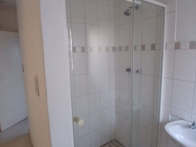 A functional bathroom featuring a glass-enclosed shower, tiled walls, and a pedestal basin, requiring some cosmetic updates to improve its overall condition.