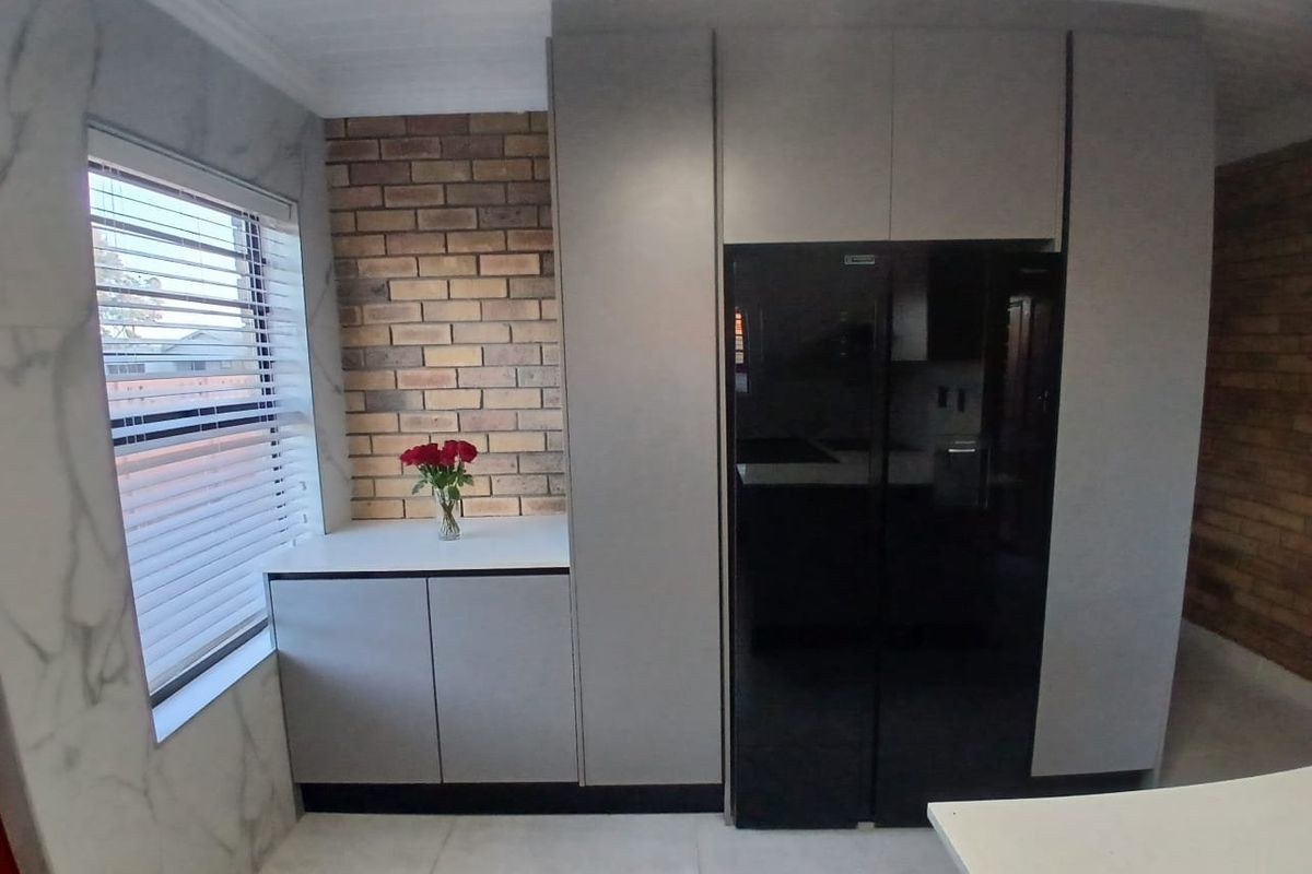 Modern kitchen area featuring sleek grey cabinetry, an exposed brick feature wall, and elegant marble-look wall tiles with large format floor tiling.