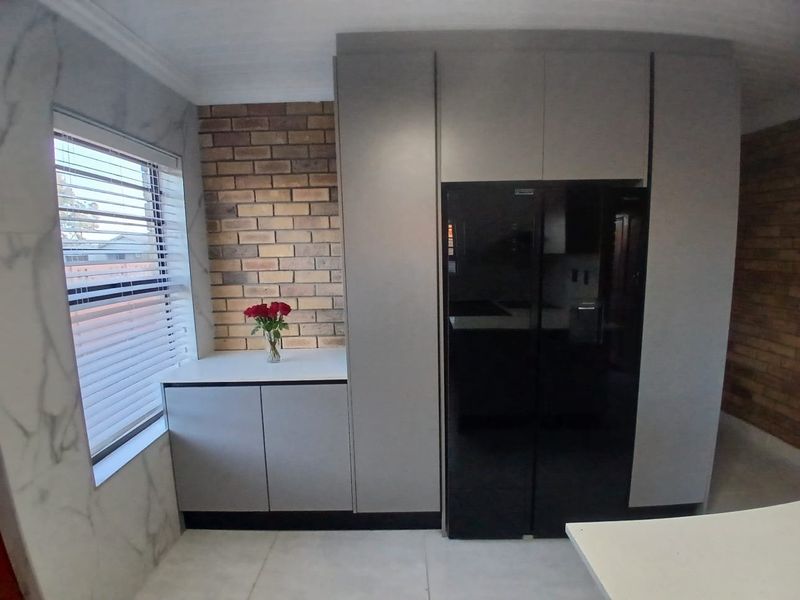 Modern kitchen area featuring sleek grey cabinetry, an exposed brick feature wall, and elegant marble-look wall tiles with large format floor tiling.