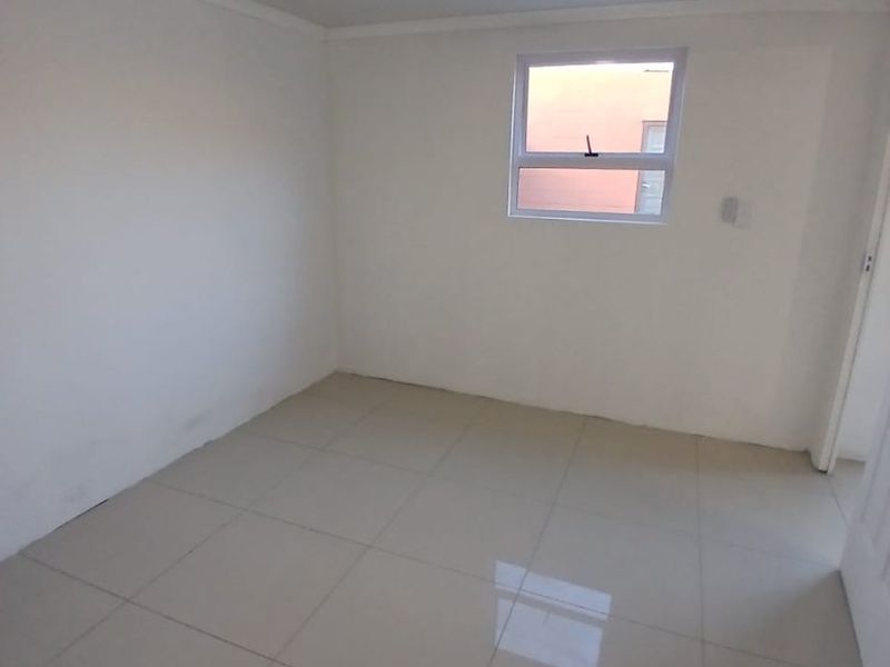 A clean, empty bedroom featuring neutral tiled flooring, a ceiling fan, and a single window, providing a blank canvas for personalization.