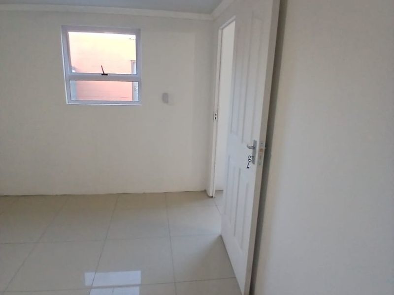 A clean, empty bedroom featuring neutral tiled flooring, a ceiling fan, and a modern aluminium window, providing a blank canvas for personalization.