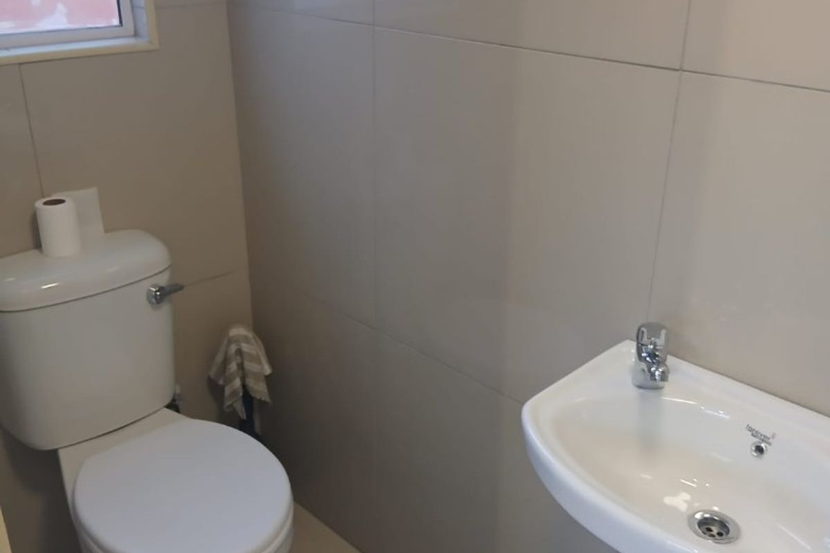 A clean and functional guest bathroom featuring neutral ceramic wall and floor tiles, a white toilet, and a wall-mounted basin.