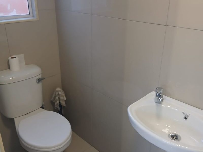 A clean and functional guest bathroom featuring neutral ceramic wall and floor tiles, a white toilet, and a wall-mounted basin.