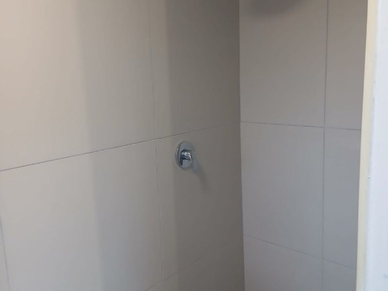 A clean, modern shower enclosure featuring neutral wall tiles, a mosaic tiled floor, and a contemporary chrome shower head and mixer.