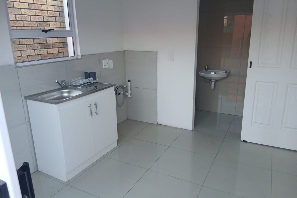 A clean, functional laundry area featuring a stainless steel sink, built-in cabinetry, and tiled finishes, with an adjacent small washroom.