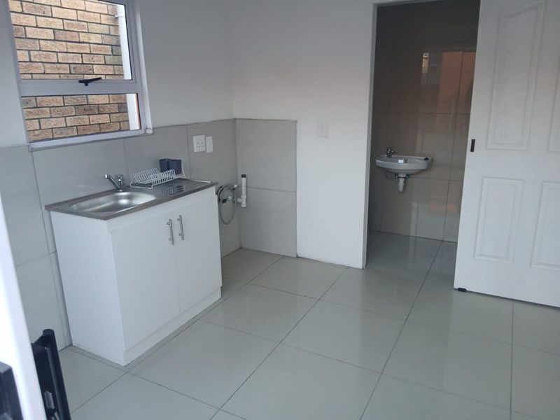 A clean, functional laundry area featuring a stainless steel sink, built-in cabinetry, and tiled finishes, with an adjacent small washroom.