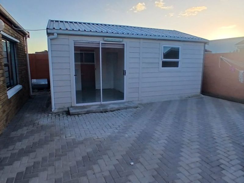 A rear view of a detached outbuilding featuring a corrugated metal roof, sliding glass door, and a paved patio area.