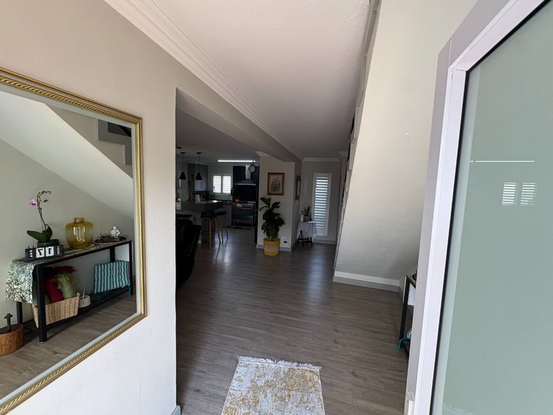 A bright and welcoming entrance hall featuring modern laminate flooring, crown molding, and a view through to the open-plan living and kitchen area.