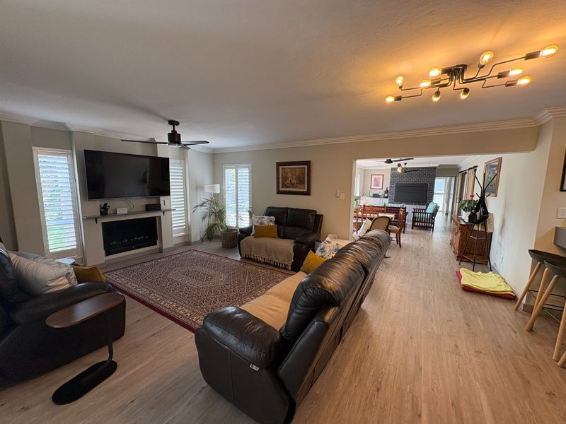Spacious open-plan living area featuring laminate flooring, a fireplace, modern lighting, and plantation shutters, creating a bright and inviting atmosphere.