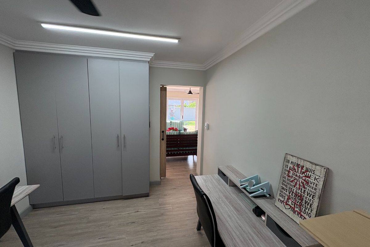A well-maintained bedroom featuring modern grey built-in cupboards, laminate flooring, and a sliding barn door leading to an adjacent living space.
