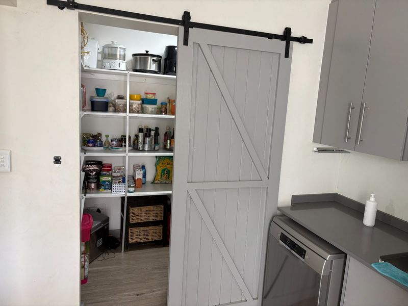 A functional scullery or pantry area featuring a modern grey sliding barn door, built-in shelving, and integrated kitchen cabinetry with a stone countertop.