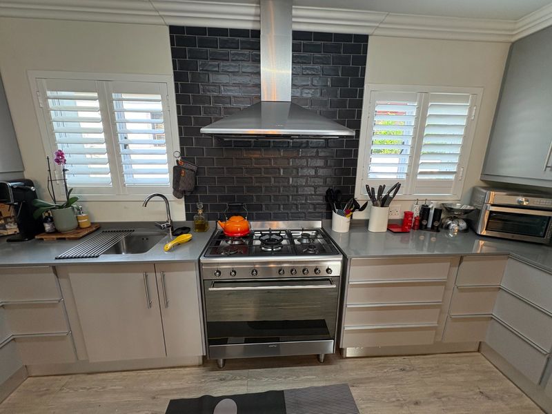 Modern kitchen featuring a stainless steel gas stove, extractor fan, subway tile backsplash, and plantation shutters, offering a clean and functional cooking space.