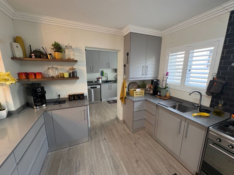 Modern kitchen featuring grey cabinetry, stone countertops, floating timber shelving, and a scullery area with additional storage and sink.