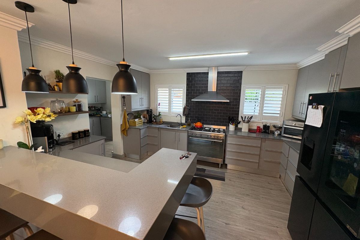 Modern kitchen featuring quartz countertops, gas stove with extractor, ample built-in cabinetry, and plantation shutters, creating a functional and stylish culinary space.