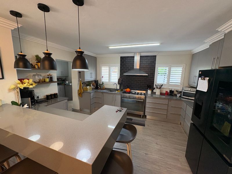 Modern kitchen featuring quartz countertops, gas stove with extractor, ample built-in cabinetry, and plantation shutters, creating a functional and stylish culinary space.