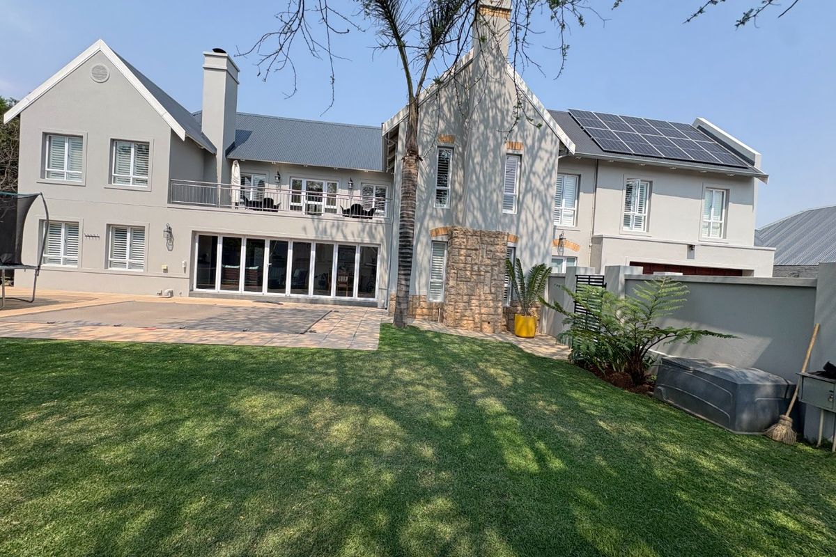 Rear view of a two-story residence featuring a paved patio, landscaped lawn, stone accents, balcony, and roof-mounted solar panels.