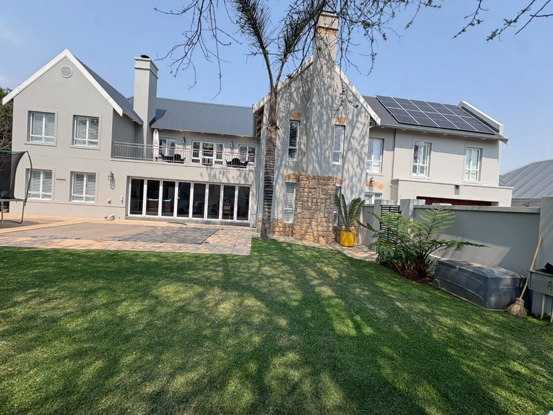 Rear view of a two-story residence featuring a paved patio, landscaped lawn, stone accents, balcony, and roof-mounted solar panels.