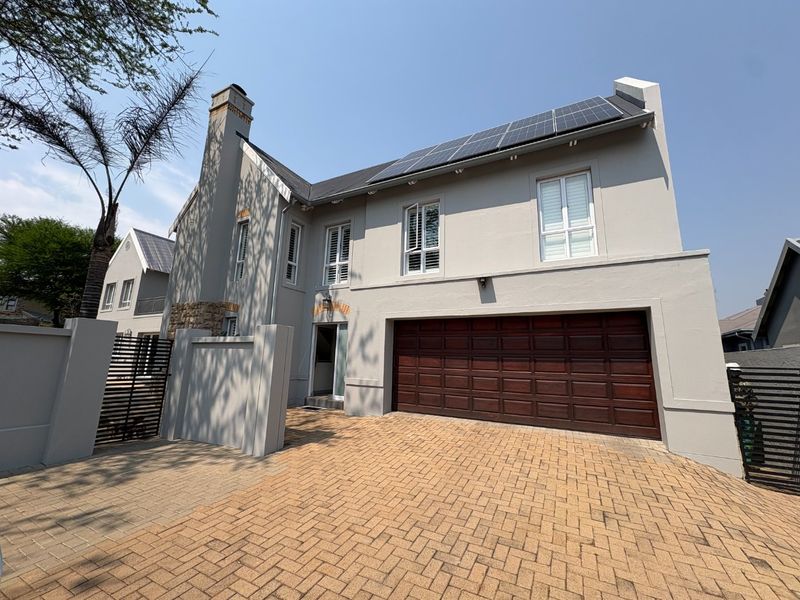 Front elevation of a modern double-story house featuring a paved driveway, double garage, and roof-mounted solar panels.