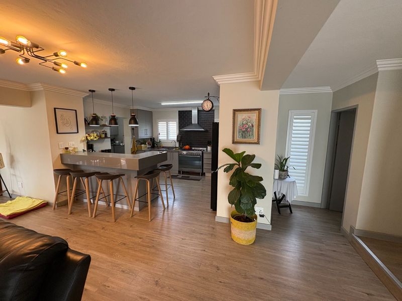 Open-plan living area featuring a modern kitchen with a breakfast bar, gas stove, extractor fan, and stylish laminate flooring throughout.