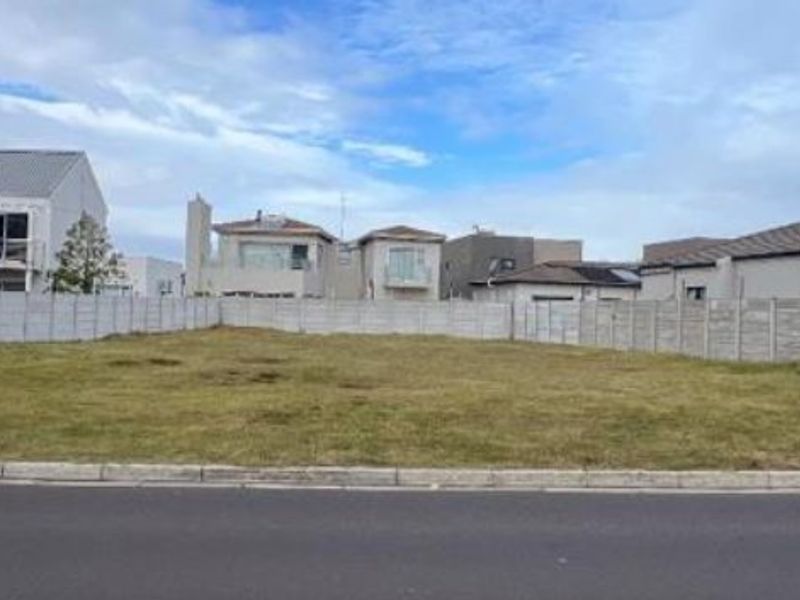 A vacant residential plot of land enclosed by precast concrete boundary walls, situated in a developed suburban street.