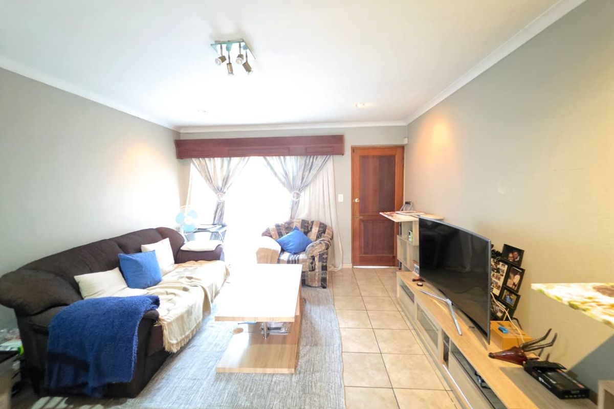 A comfortable living room featuring tiled flooring, neutral wall finishes, and a timber door leading to an outdoor area.