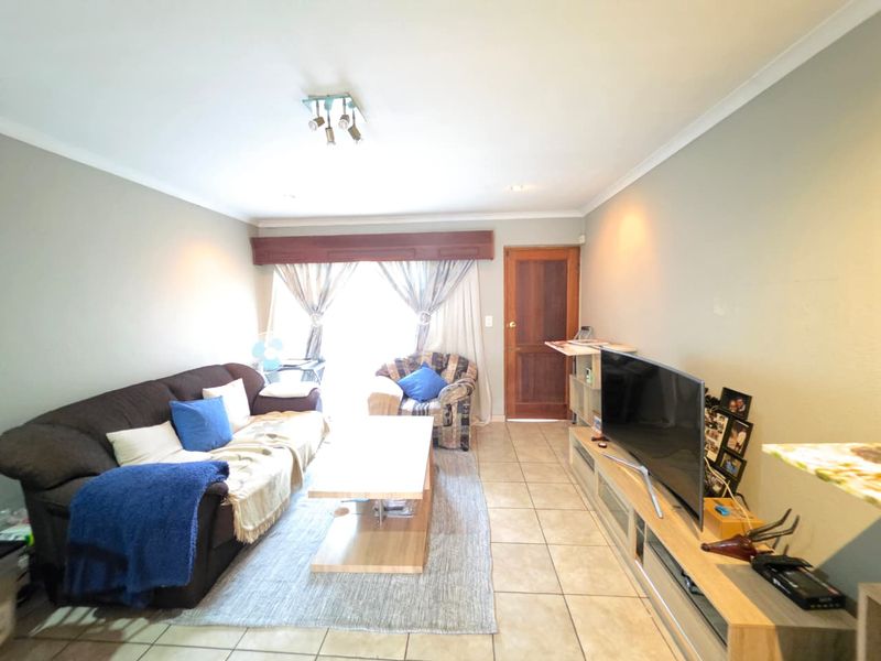 A comfortable living room featuring tiled flooring, neutral wall finishes, and a timber door leading to an outdoor area.