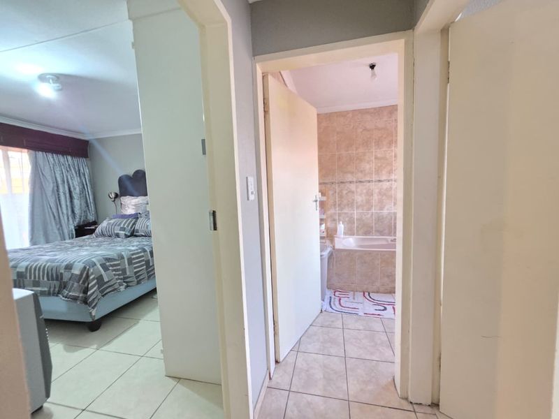 A hallway view connecting a bedroom and a bathroom, featuring neutral tiled flooring and standard interior door frames.
